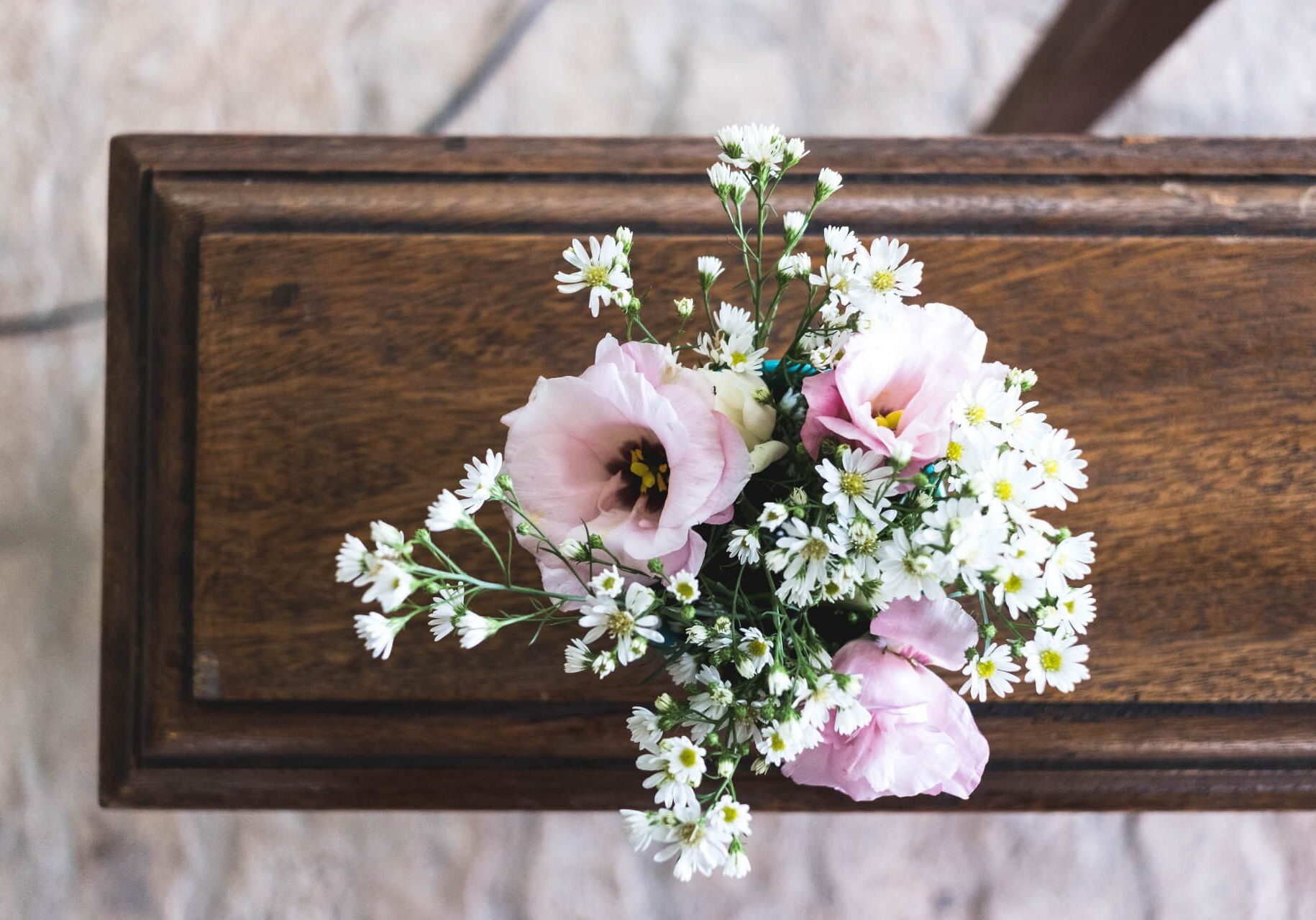 A posy of blush lisianthus and white daisies laid on a coffin