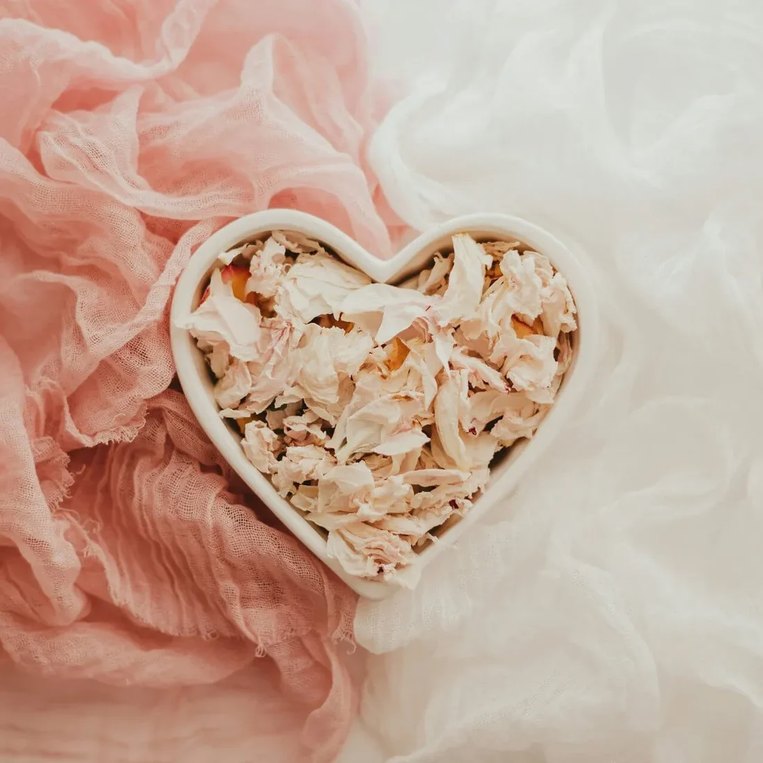 Dried petals in a heart-shaped dish on blush linen